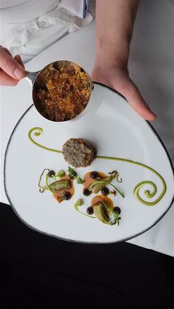 Elegant plated dish with intricate green sauce swirls, small greens, and a refined meat centerpiece at restaurant Daniel.