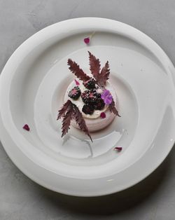 Fine dining dessert featuring a small mousse cake topped with blackberries, cream, purple edible flowers, and red leaves on a