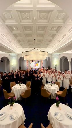 Spacious dining room with round tables, brown chairs, elegant white decor, and restaurant staff posing together.