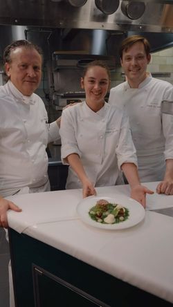Three chefs in a professional kitchen presenting a plated gourmet dish at Daniel restaurant.