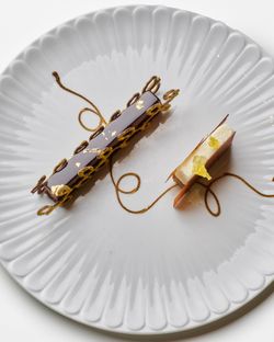 Two intricately plated rectangular desserts with chocolate and cream, garnished with gold leaf and decorative swirls on a fln