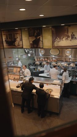 Busy kitchen scene at Daniel featuring chefs in white uniforms preparing dishes and staff coordinating plating in a fine-dine