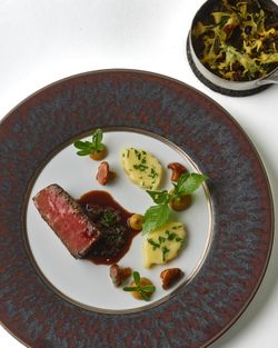 Fine dining dish with seared meat, sauce, herbs, mushrooms, and a side of crispy vegetables at Daniel restaurant.