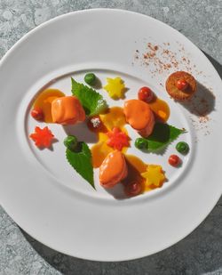 Three pieces of food with orange sauce, star-shaped vegetables, and green leaves arranged on a white plate at Daniel French. 