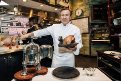 Chef holding a cooked bird in a professional kitchen at Daniel, a Michelin star French restaurant in NYC.