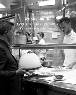 Busy kitchen scene at Michelin French restaurant Daniel with chefs preparing dishes and a server holding a cloche.
