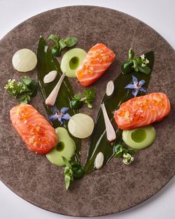 Plated fine dining dish with seared salmon, green sauce, herbs, and edible flowers on a textured plate.