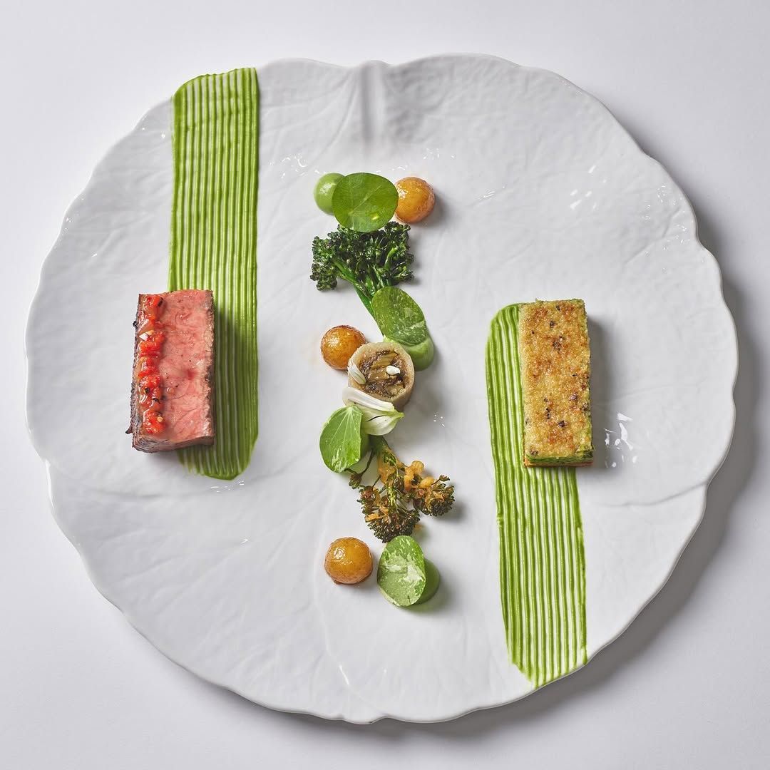Plated dish featuring sliced beef, vibrant green sauce, and decorative vegetable elements on an elegant white plate.