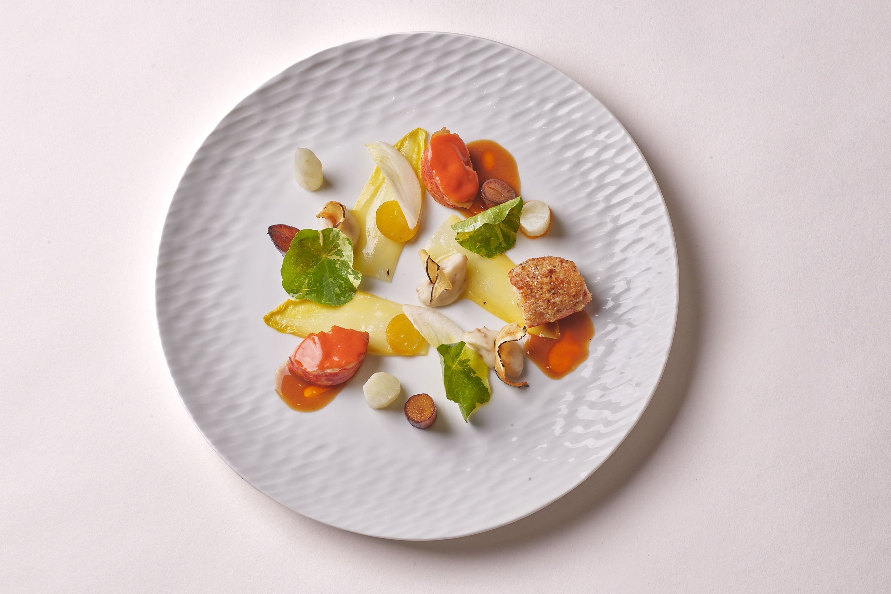 A gourmet dish featuring colorful vegetables and sauces, artistically arranged on a textured white plate.