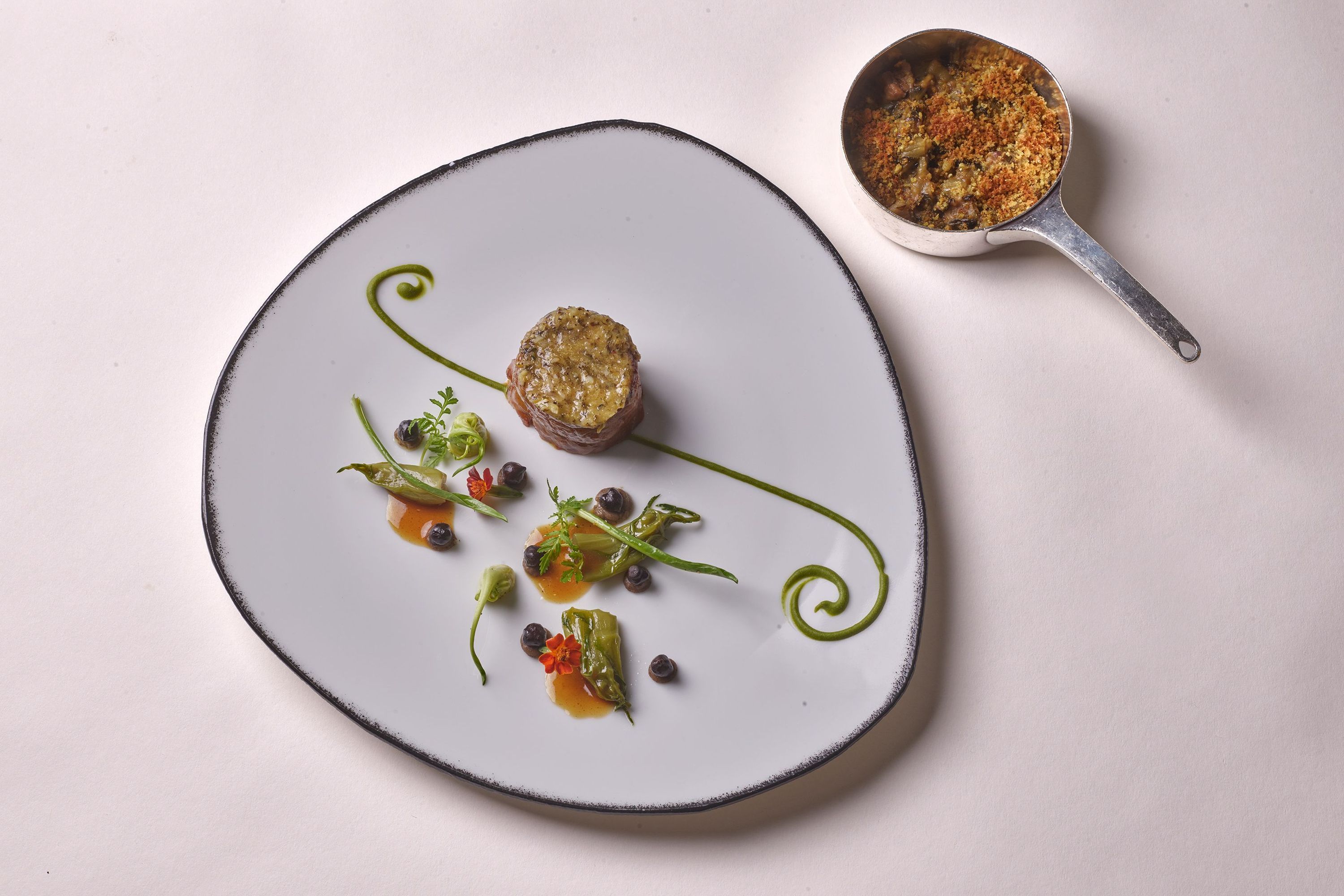 A gourmet dish presented on an elegantly shaped plate, featuring a circular patty and garnishes.